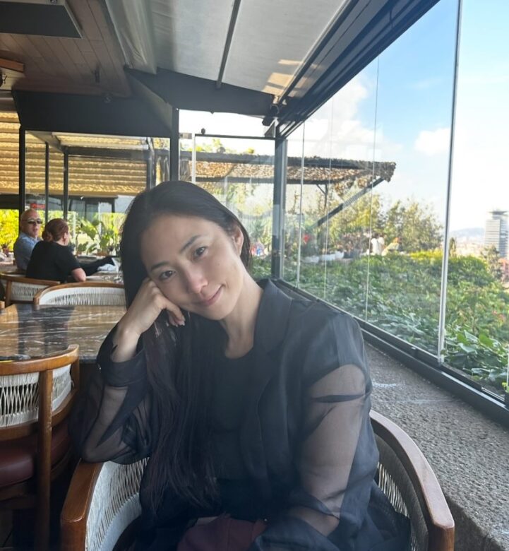 椅子に座り海外の風景をバックに微笑むMEGUMI