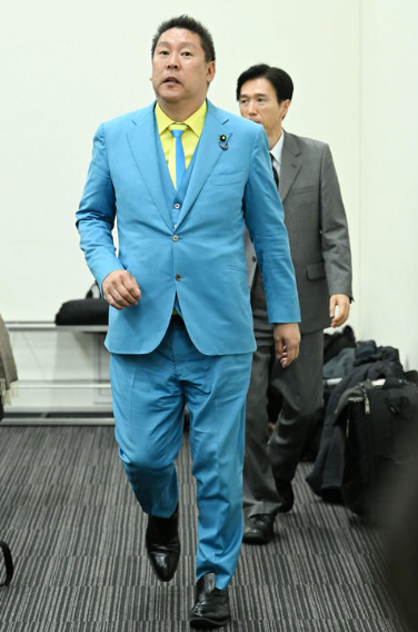 上下ブルーと黄色いワイシャツの派手な立花孝志