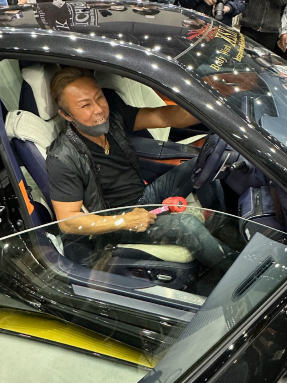高級車に乗りポーズをとる薬師寺保栄